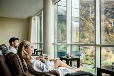 a woman sitting on a couch with a cup of coffee at Hotel Union Geiranger Bad & Spa in Geiranger