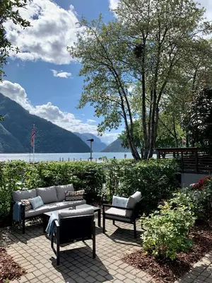 a patio with a couch and chairs next to a lake at Klingenberg Hotel - Årdal in Årdalstangen