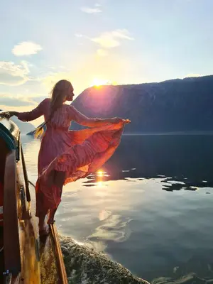 a woman standing on the edge of a boat on a lake at Klingenberg Hotel - Årdal in Årdalstangen