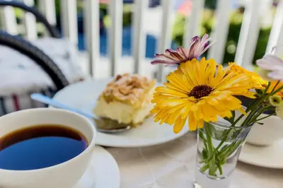 a cup of coffee and a plate of cake and a vase of flowers at Vik Pensjonat in Eidfjord
