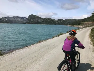a woman riding a bike on a dirt road next to a lake at Geilo Superior leilighet in Geilo