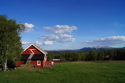 a red barn in a field with mountains in the background at Bustad Hyttetun in Skåbu