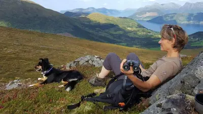 a man holding a camera and a dog on a hill at Cosy chalet, 100m2 with fjordview! in Lauvstad