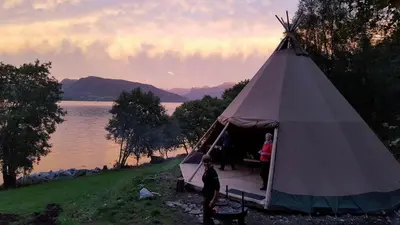 a group of people standing inside of a tent by the water at Tiny house with Fjordview! in Lauvstad