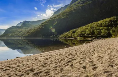 a beach next to a body of water with mountains at Ingrids Apartments in Eidfjord