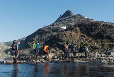 a group of people crossing a river with a mountain in the background at Sommerhotellet in Vang I Valdres