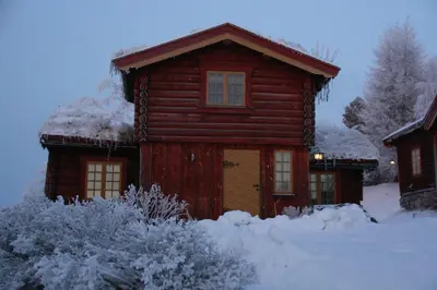 a log cabin with snow on the front of it at Romenstad Hytter in Rendalen