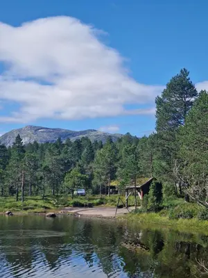 a cabin by a lake with mountains in the background at Hov Hyttegrend in Viksdalen