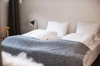 a bed with white sheets and a blue blanket on it at Lindstrøm Hotel in Lærdalsøyri