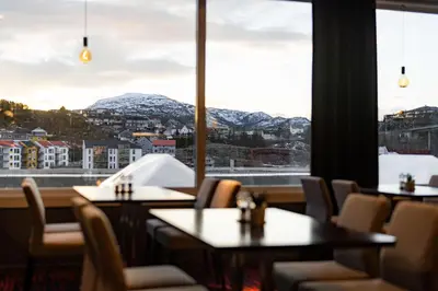 a restaurant with tables and chairs and a view of mountains at Scandic Kristiansund in Kristiansund