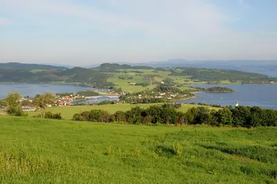 a green field with a view of a town and a lake at Husfrua Gårdshotell in Straumen