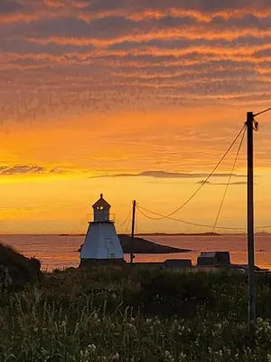 a lighthouse on the shore of the ocean at sunset at Vestavind hytter og rom AS in Ålesund