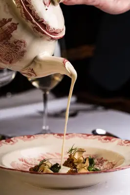 a person is pouring sauce into a plate of food at Geilo Mountain Lodge in Geilo
