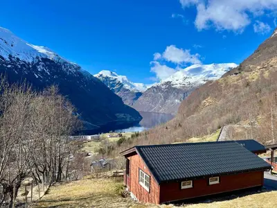 a small red building with mountains in the background at Fossen Accommodation in Geiranger