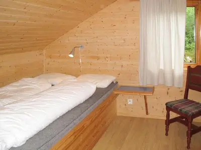 a large bed in a wooden room with a chair at Chalet Julie by Interhome in Eikelandsosen