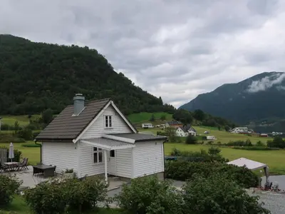 a small white house with mountains in the background at Holiday Home Ikjefjord by Interhome in Bjordal