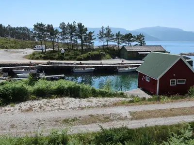 a red barn and a dock with boats in the water at Holiday Home Solsvika by Interhome in Leirvik