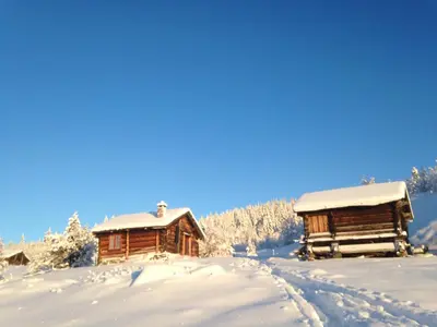 two wooden cabins with snow on the ground at Nilsrud 30 Feriehus in Åmotsdal