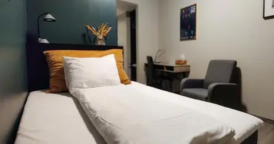 a bed with white sheets and an orange pillow and a chair at Hotell Molde in Molde