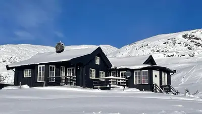 a black house in the snow with snow covered mountains at Veslehytta - cabin 1050 moh via amazing view and ambiance in Ål