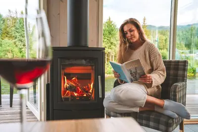 a woman sitting on a couch reading a book in front of a fireplace at Topcamp Hallingdal - Ål in Ål
