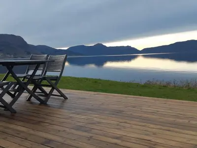 a picnic table and bench on a deck overlooking a lake at feriehus ved sjøen in Tomrefjord