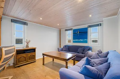 a living room with blue couches and a wooden ceiling at Sveggvika Guesthouse in Averoy
