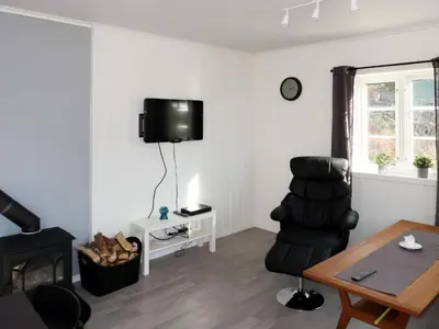 a living room with a chair and a tv on the wall at Holiday Home Nesholmen by Interhome in Leirvik