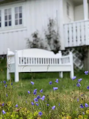 a white bench in front of a white house with purple flowers at Pålberget in Råkvåg