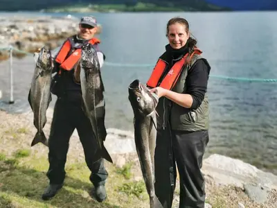 a couple of people holding fish in front of a body of water at 5 person holiday home in EIDSVÅG in Eidsvåg
