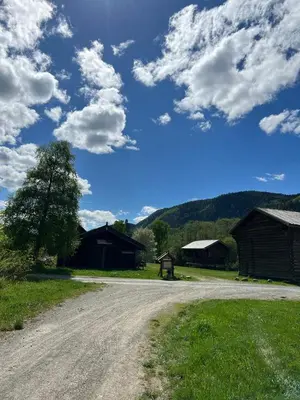 a dirt road in a field with buildings and a sky with clouds at Sevletunet B&B and Cabins in Rødberg