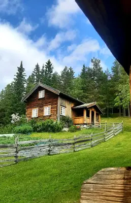 a wooden house in a field next to a fence at Gamlestugu Greivjord Fjellgard in Tuddal