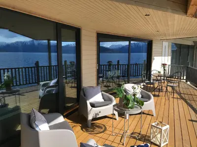 a porch with chairs and tables and a view of the water at Panoramaresort in Hardangerfjorden leilighet i sjøkanten ved Hardangerfjorden for 7 personer boat , sauna,kajak, SUP for rent in Øystese
