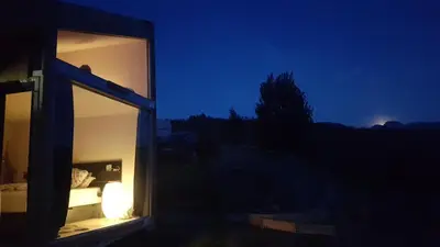 a room with a window with a bed in it at night at Hardanger Fjordtun PANORAMA cabin near the Hardangerfjord with fantastic fjordview, silence and nature in Herand