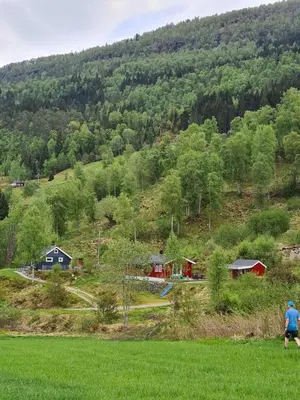 a man standing in a field in front of a hill at Nordfjordcabins RED in Utvik