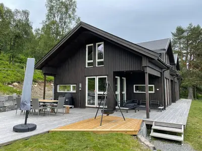 a black house with a wooden deck with a table at Lykkeli in Stranda