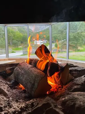 a fire pit with logs in front of a window at Melkevoll Bretun Camping in Briksdalsbre