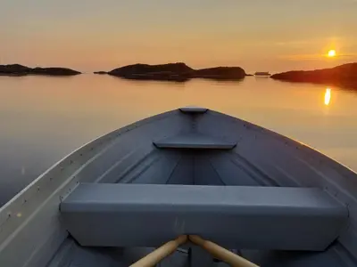 a boat in the water with the sunset in the background at Vollvaagen Apartments Smøla, boat included in Smøla