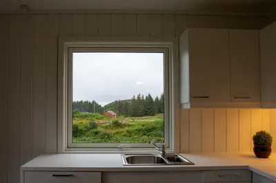 a kitchen with a window over a sink and a field at Vollvaagen Apartments Smøla, boat included in Smøla