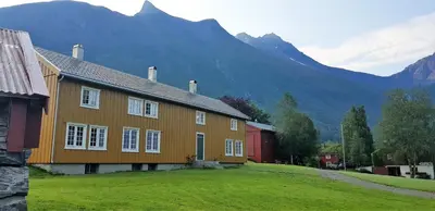 a house on a field with mountains in the background at Lensmansgarden Marteinsgarden in Innfjorden