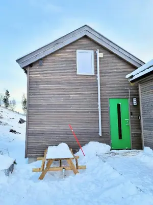 a building with a green door and a picnic table in the snow at Tiny mountain cabin with a panoramic view in Giljane