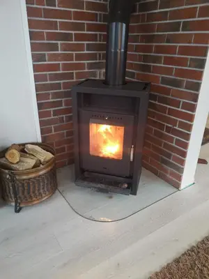 a wood stove in a brick fireplace with a basket at Utleiebolig Fannrem in Fannrem