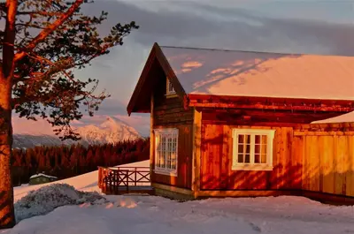 a small wooden house in the snow with a tree at Løstegård Cabins in Gol