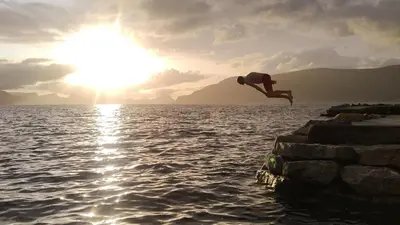 a man jumping off a pier into a body of water at Småstranda Fjord Lodge in Åheim