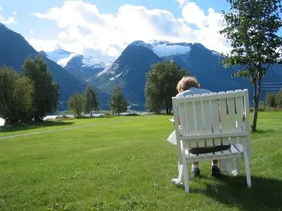 a woman sitting on a white bench looking at the mountains at Hjelle Hotel in Hjelle