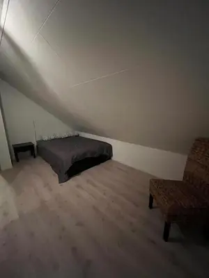 a bedroom with a bed and a chair in a attic at Hjelvikhytta - flott beliggenhet ved sjøen in Hjelvik