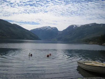 two people swimming in a lake with a boat at Seim Camping - Røldal in Røldal