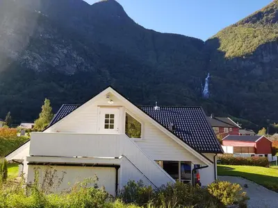 a white house with a garage in front of a mountain at Bright and cozy apartment 1.5km from city centre in Aurland