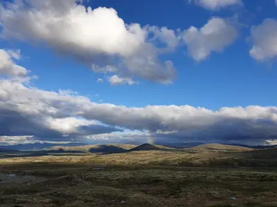 a rainbow in the sky over a field with mountains at Snøhetta Camping in Hjerkinn