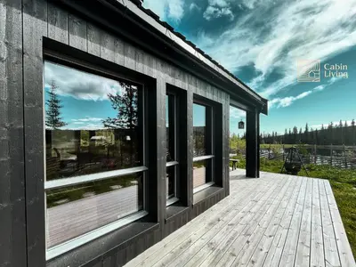 a house with large windows on a wooden deck at Unique cabin with fantastic lake view, sauna, ski & EV outlet in Svingvoll